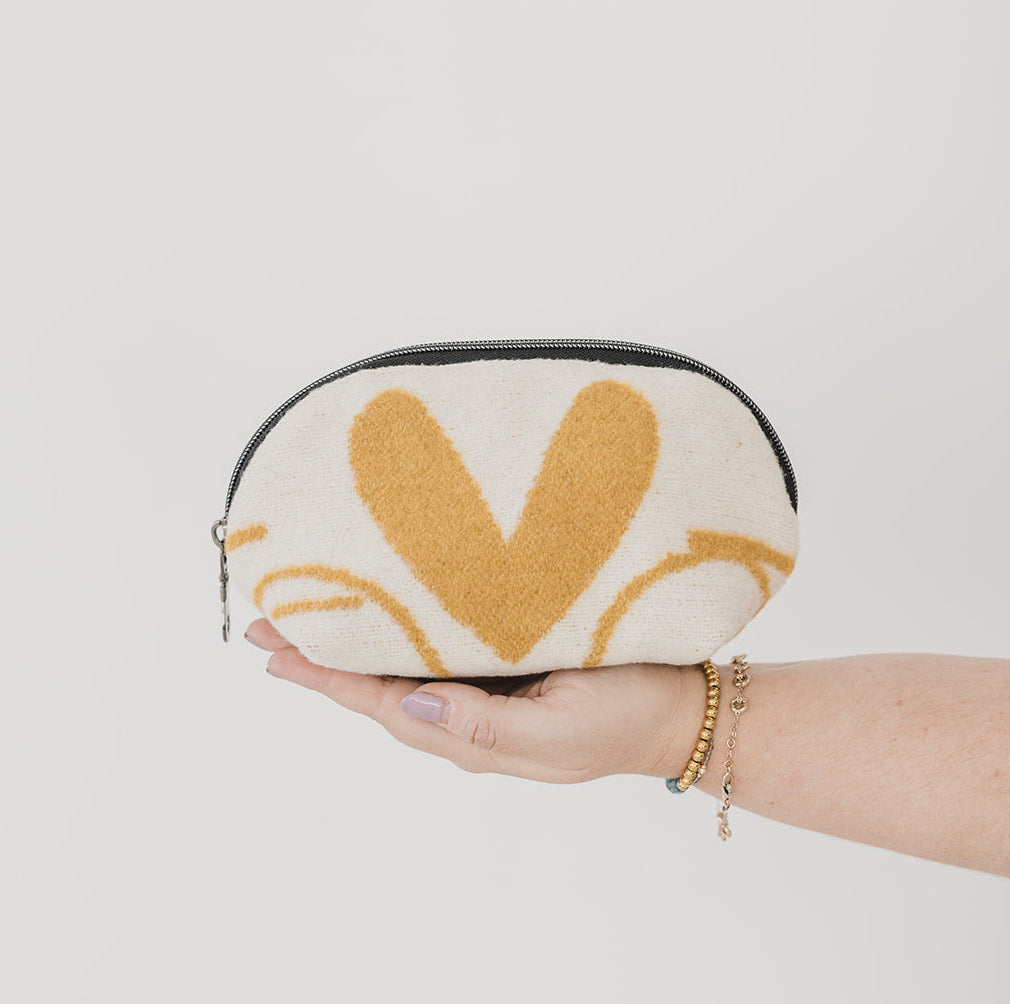 Hand holding a small pouch with a yellow heart design on a plain background